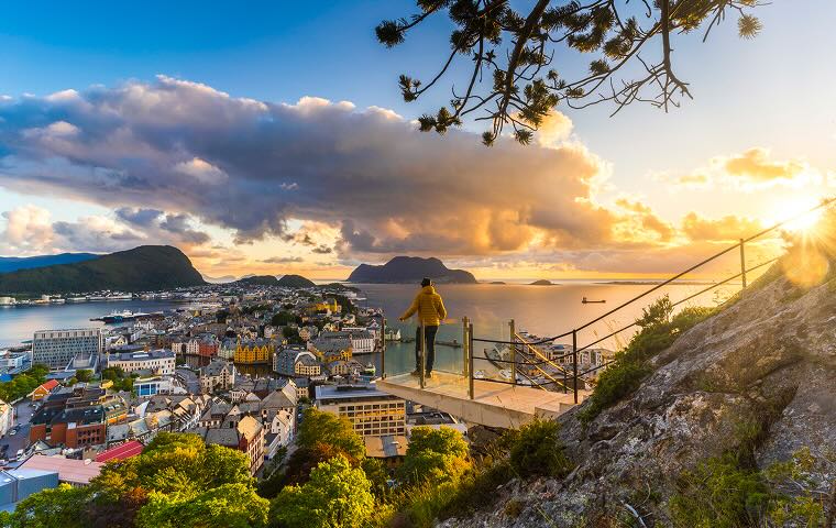 A person standing on a lookout overlooking a city at sunset